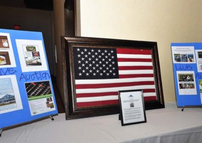 American flag displayed in a frame, flanked by two informational posters about live auctions on easels in a room.