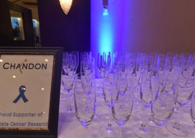 Rows of empty champagne glasses beside a chandon sign indicating support for prostate cancer research at an event.