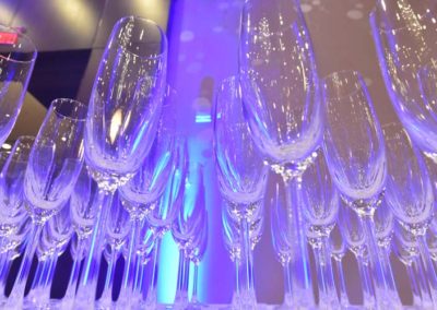Row of empty champagne glasses arranged on a bar with blue lighting in the background.