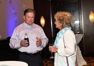 A man holding a beer bottle converses with a woman holding a wine glass at an indoor event.