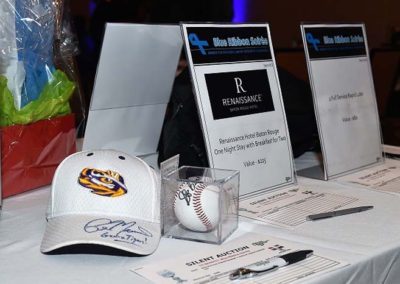 Table display with silent auction items, including an autographed baseball cap and signage with bid sheets.