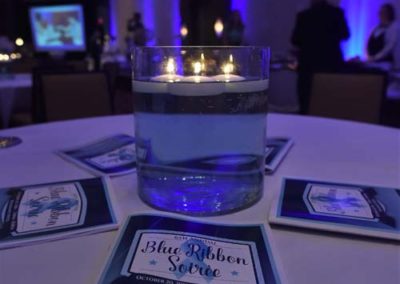 A candlelit table with event brochures at a blue ribbon soiree in a dimly lit banquet hall.