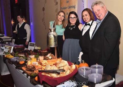Four people smiling at a catering event with a table full of food in the foreground.