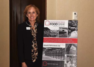 A woman smiling next to a promotional stand for a food bank at an indoor event.