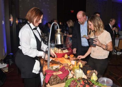 A woman serving cheese and fruit to guests at a buffet during an indoor event.