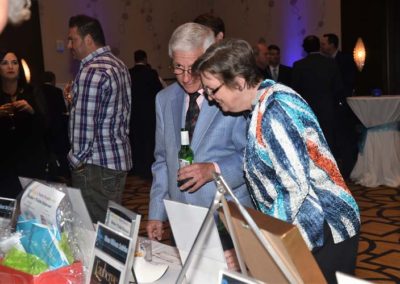 Two elderly individuals examining auction items at a formal event, with other guests visible in the background.