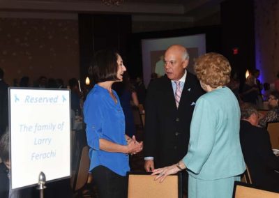 Three people conversing at a formal event near a table with a sign reading "reserved for the family of larry ferachi.