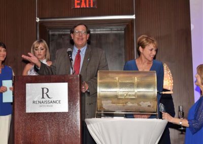 A man in glasses speaks at a podium marked "renaissance" during a raffle event, with four people around him looking at a draw box.