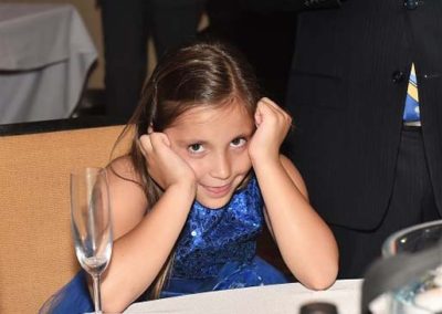 Young girl in a blue dress covering her ears at a formal event table.