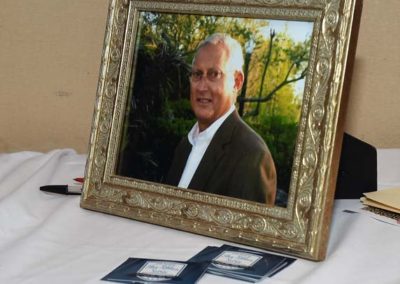 A framed photograph of a smiling older man, set on a table beside several small photo slides.