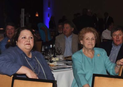 Two women and two men seated at a dining table during an event, with dim blue lighting in the background.