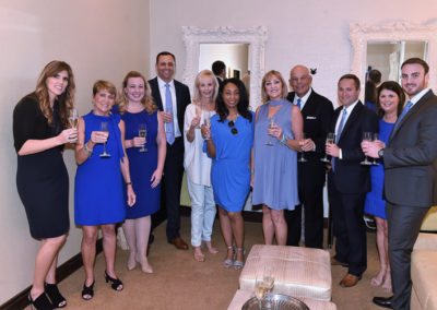 Group of ten adults in formal attire, toasting with champagne glasses in a room with elegant decor.