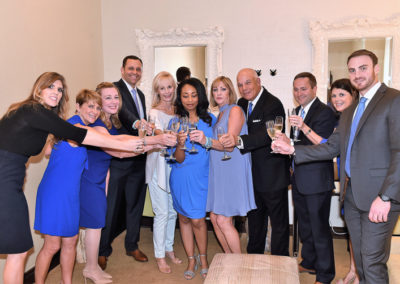 Group of ten adults in business attire toasting with champagne glasses in a warmly lit room.