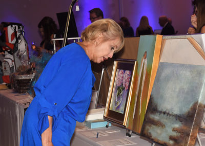 A woman in a blue dress examines paintings at an auction event.