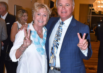 A senior couple happily posing with peace signs at a formal event in a ballroom.