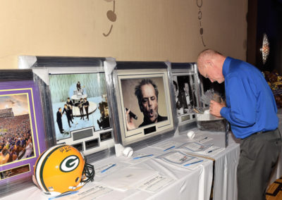 A man examines silent auction items including framed celebrity photos and a green bay packers helmet.