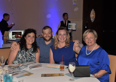 Four adults smiling at a table during an event, with drinks and event programs in front of them.