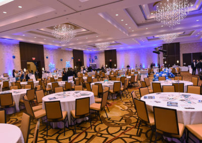 Elegant banquet hall setup for an event with round tables, blue decorations, and modern chandeliers.