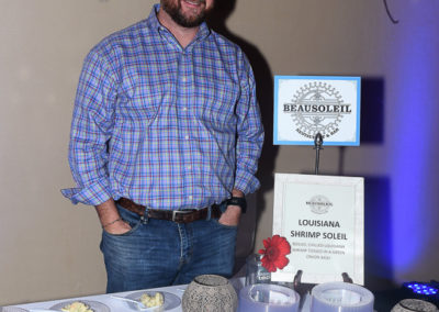 Man standing beside a table displaying louisiana shrimp dishes and promotional materials at an event.