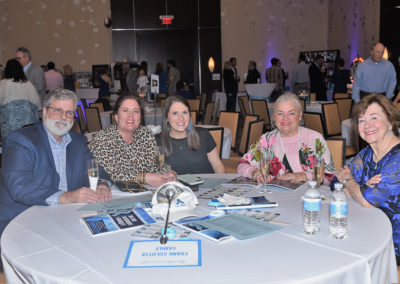 Five people smiling at a table during a formal event with event brochures and water bottles visible on the table.