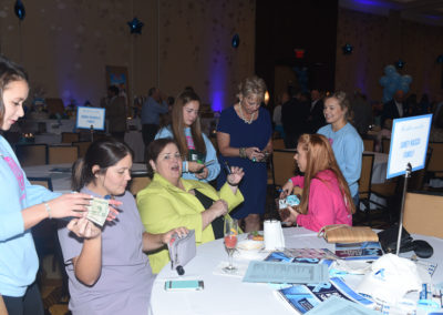 Group of women interacting and exchanging business cards at a networking event with tables decorated in blue.