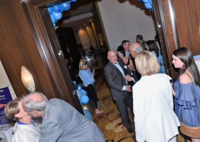 People conversing at a networking event in a hotel hallway decorated with blue balloons.