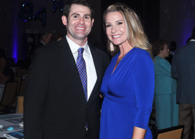 A man and a woman posing together at a formal event, both smiling for the camera. the man in a black suit and the woman in a blue dress.