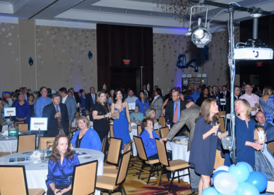 A crowd of people in formal attire attending an indoor event with blue lighting and decorations.