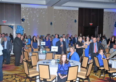 People in formal attire attending an event in a ballroom with blue and silver decorations.