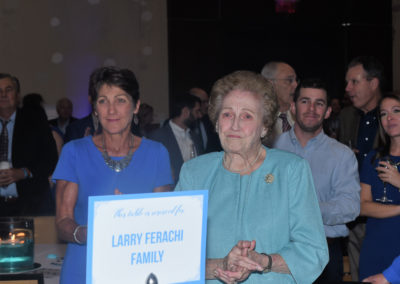 Two women standing beside a sign that reads "larry ferachi family" at a formal event, with attendees in the background.