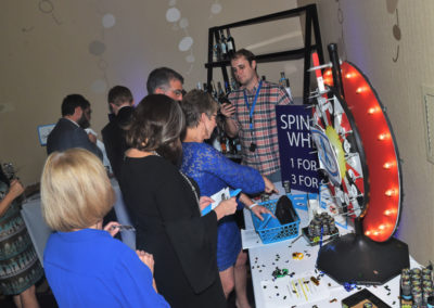 People gather around a prize wheel at an indoor event, engaging in conversation and participating in a game.