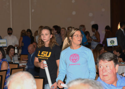 Two women, one in an lsu gymnastics t-shirt and the other in a jimmy buffett's margaritaville sweatshirt, standing in a crowded event hall.