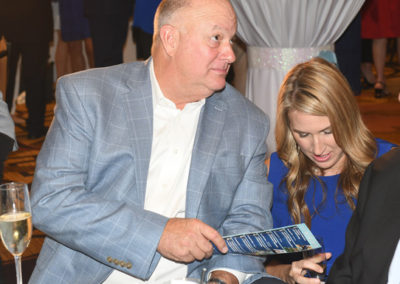A man in a gray suit and a woman in a blue dress look at a booklet together at a formal event.