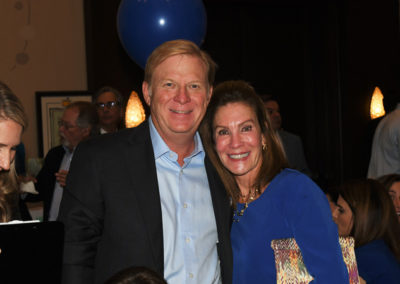 A smiling man and woman posing together at an indoor event, with a blue balloon floating in the background.