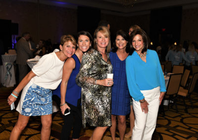 Five women posing together with smiles at an indoor event, dressed in casual and semi-formal attire.