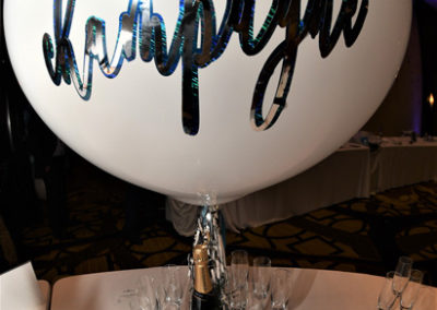 A large balloon with "champagne" written on it, above a bottle and glasses on a table, ready for a celebration.