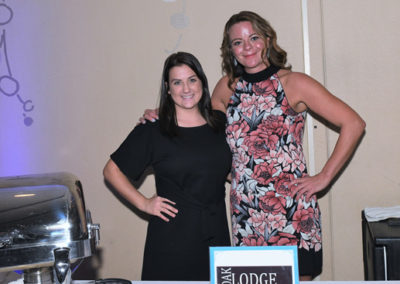 Two women smiling and standing beside a buffet table with a sign reading "slodge" at an event center.