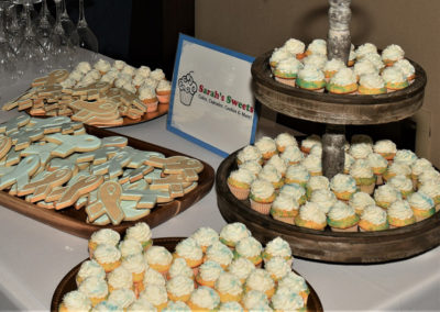 Assorted cookies and cupcakes on wooden display stands at an event, with a sign reading "sarah's sweets.