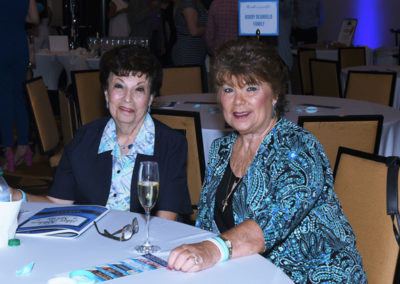 Two older women smiling at a table with a champagne glass during an event in a banquet hall.