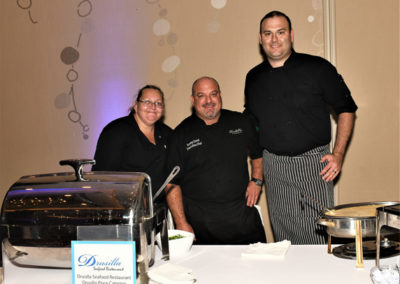 Three chefs standing behind a catering station with a chafing dish at a restaurant event.
