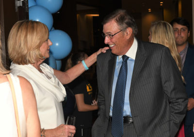 Woman touching the cheek of a smiling man in a suit at a party with blue balloons in the background.