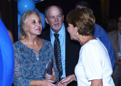 Three adults engaged in a conversation at a social event with blue balloons in the background.