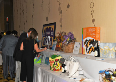 People browsing items at a charity auction event with various baskets and goods displayed on a table.