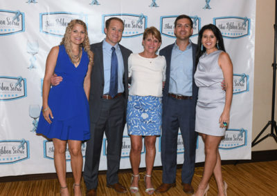 Five adults smiling at a formal event with a "blue ribbon soiree" banner in the background.