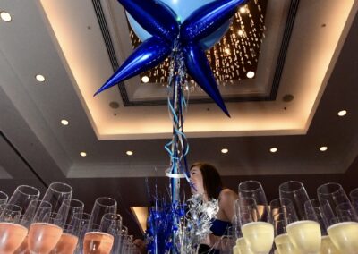 Large balloon labeled "champion" above a display of glasses filled with champagne, with blue star-shaped decorations and a woman in the background.