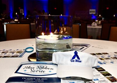 A candle centerpiece at a "go blue" themed event with informational pamphlets and a cap on a table.