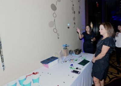 Two women interacting at a table with party decorations and cups at an indoor event, one is throwing a confetti.