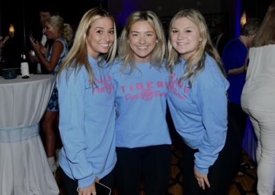 Three young women smiling in matching blue t-shirts at an indoor event.