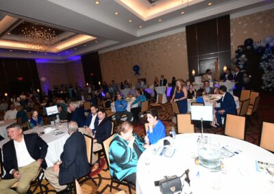 Guests seated at round tables in a decorated banquet hall during a formal event with blue and silver balloons.