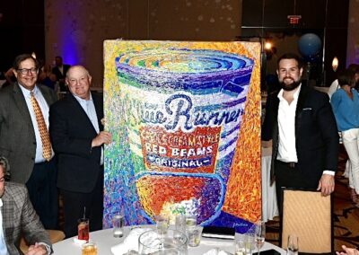 Four men standing next to a colorful painting of a blue runner red beans can at a gala event.